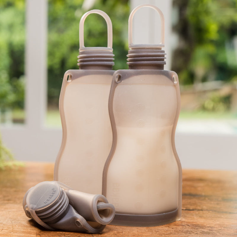 Three Silicone Milk Storage Bags on a wooden table, two filled with milk, one empty and rolled up.