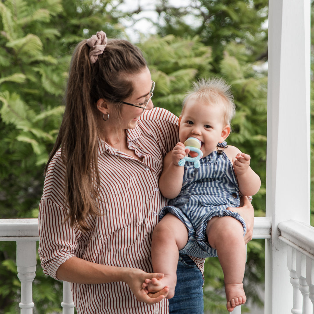 A mother holding her baby who is using the Haakaa Fresh Food Feeder